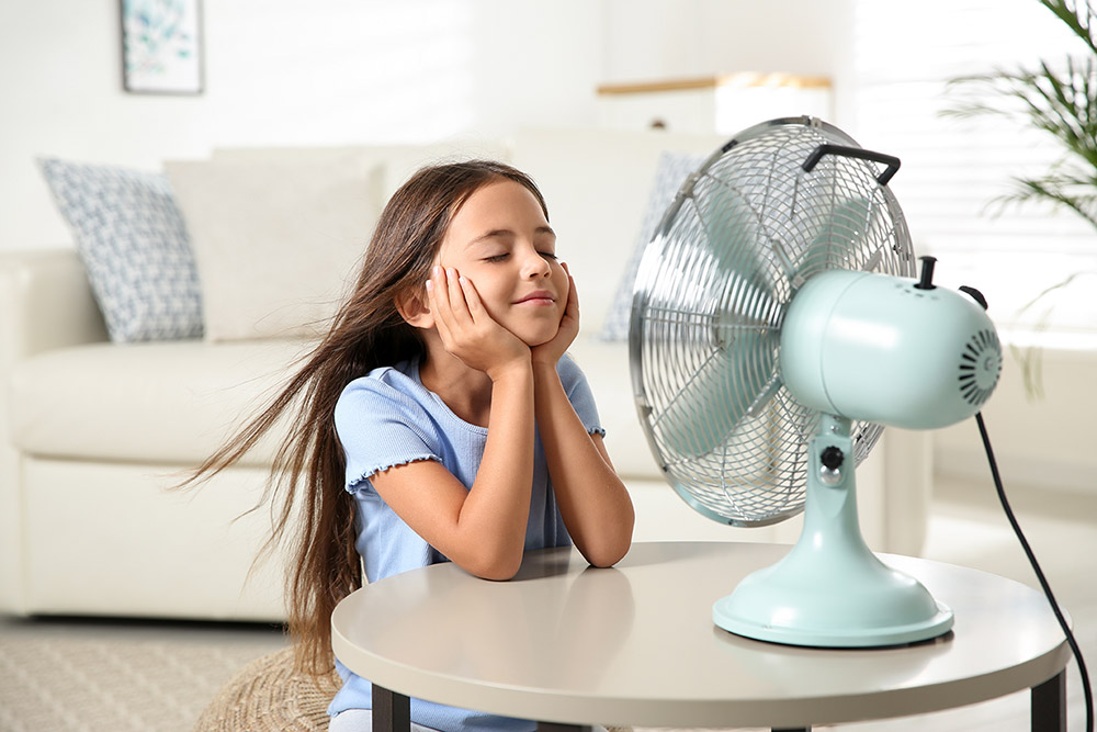 Woning of gebouw koel houden met ventilator, klein meisje geniet in woonkamer van wind ventilator